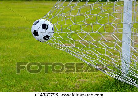 Stock Photograph - Close-Up of a Football Trapped in a Goal Net on a Football Pitch. Fotosearch