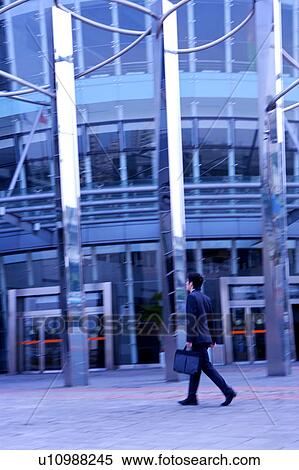 Businessman walking in front of office building View Large Photo Image Stock Photography - Businessman walking in front of office building. Fotosearch
