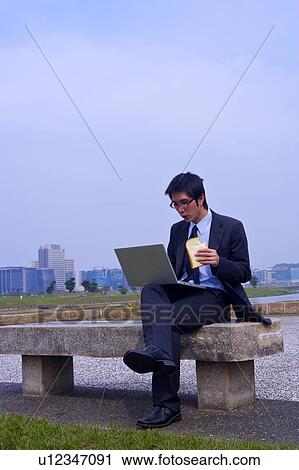 Young businessman eating toast while using laptop View Large Photo Image Stock Image - Young businessman eating toast while using laptop. Fotosearch