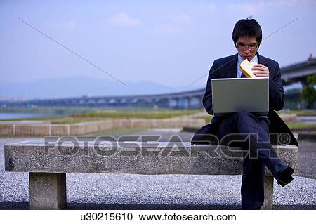 Young businessman eating toast while using laptop View Large Photo Image Stock Image - Young businessman eating toast while using laptop. Fotosearch