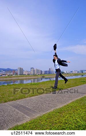 Picture - Young businessman holding briefcase jumping in park. Fotosearch