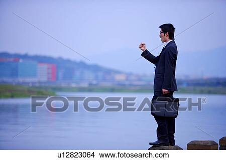 Young businessman holding briefcase standing at water's edge View Large Photo Image Picture - Young businessman holding briefcase standing at water's edge. Fotosearch