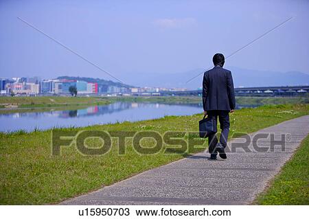 Young businessman holding briefcase walking on footpath View Large Photo Image Stock Image - Young businessman holding briefcase walking on footpath. Fotosearch