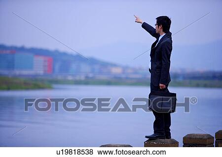 Young businessman holding briefcase pointing at distance View Large Photo Image Stock Photo - Young businessman holding briefcase pointing at distance. Fotosearch