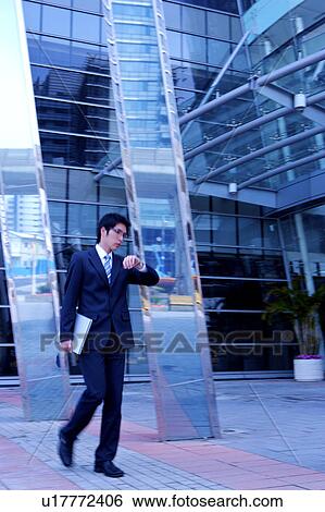 Young businessman holding laptop looking at watch, office building in the background View Large Photo Image Stock Photograph - Young businessman holding laptop looking at watch, office building in the background. Fotosearch