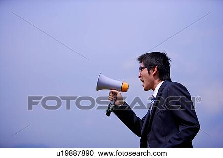 Young businessman holding megaphone against blue sky View Large Photo Image Stock Image - Young businessman holding megaphone against blue sky. Fotosearch