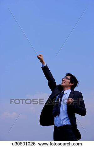 Young businessman punching the air, against blue sky View Large Photo Image Stock Photograph - Young businessman punching the air, against blue sky. Fotosearch