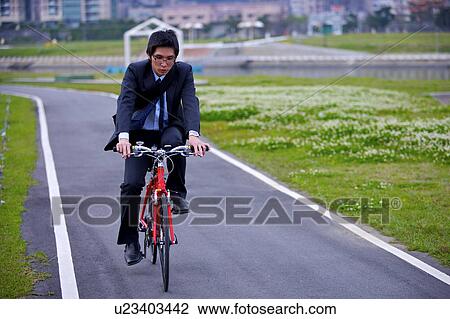 Stock Image - Young businessman riding bike outdoors. Fotosearch