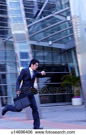 Stock Photograph - Young businessman running while watching watch. Fotosearch
