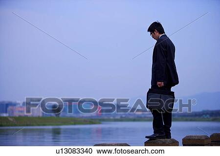 Stock Image - Young businessman standing at water's edge. Fotosearch