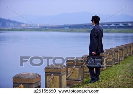 Stock Image - Young businessman standing at water's edge. Fotosearch