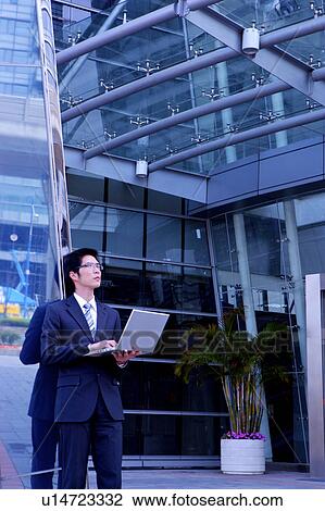 Young businessman using laptop under office building View Large Photo Image Stock Image - Young businessman using laptop under office building. Fotosearch