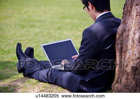 Young businessman using laptop under tree View Large Photo Image Stock Photography - Young businessman using laptop under tree. Fotosearch