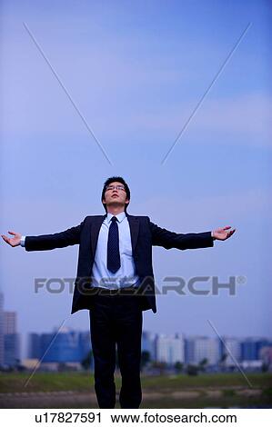 Stock Image - Young businessman with arms outstretched outdoors. Fotosearch