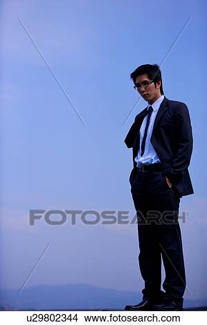 Young businessman with hands in pockets against blue sky View Large Photo Image Picture - Young businessman with hands in pockets against blue sky. Fotosearch