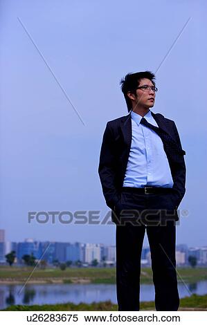 Stock Photography - Young businessman with hands in pockets, buildings in the background. Fotosearch
