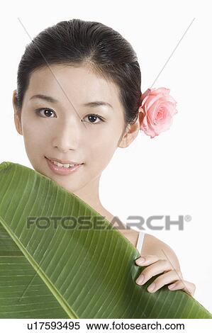 Stock Photography - "Young woman holding banana leaf with a flower, portrait". Fotosearch