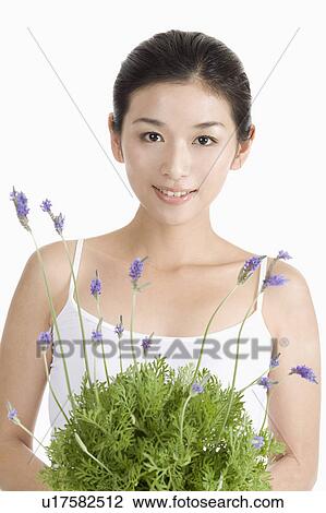 Stock Image - "Young woman holding lavender and looking at the camera, portrait". Fotosearch