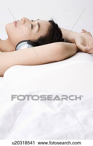 Stock Image - Young woman listening to music and lying with eyes closed. Fotosearch