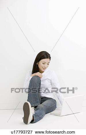 Stock Photo - Young woman sitting and using laptop. Fotosearch
