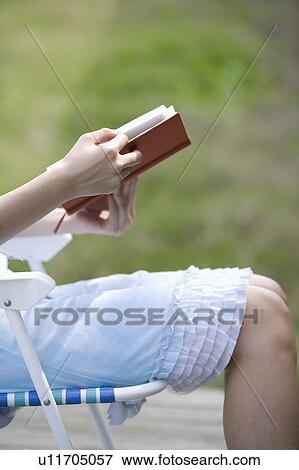 Stock Photo - Young woman sitting on armchair and reading book. Fotosearch