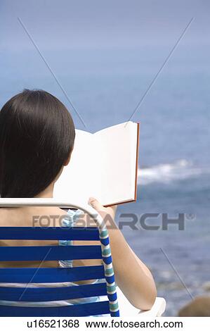 Stock Photo - Young woman sitting on armchair and reading book. Fotosearch