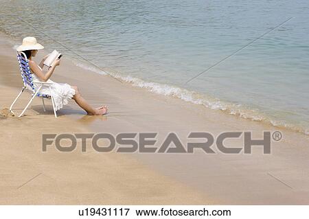 Young woman sitting on beach chair and reading book View Large Photo Image Stock Photo - Young woman sitting on beach chair and reading book. Fotosearch