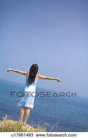 Stock Image - "Young woman standing with arms outstretched, rear view". Fotosearch