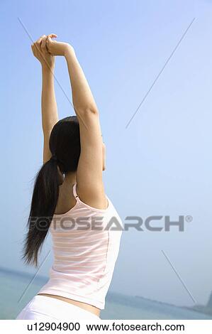 Stock Image - "Young woman stretching and looking away, rear view". Fotosearch