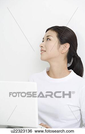 Stock Photograph - Young woman using laptop and looking away. Fotosearch