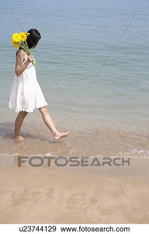 Stock Photo - Young woman walking on beach and holding sunflowers. Fotosearch