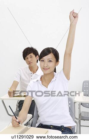 Stock Photo - Schoolboy and schoolgirl sitting in the classroom with arms raised. Fotosearch