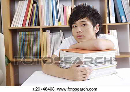 Stock Photo - "Schoolboy sitting with a stack of books and looking at the camera, portrait". Fotosearch