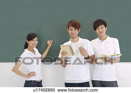 Stock Photography - Schoolboys and schoolgirl standing near blackboard and smiling at the camera. Fotosearch