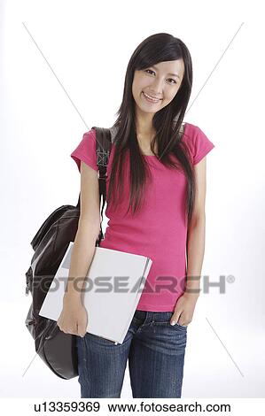 Stock Photo - Schoolgirl standing with book and school bag. Fotosearch