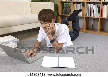 Stock Image - Teenager boy using laptop and lying on front. Fotosearch