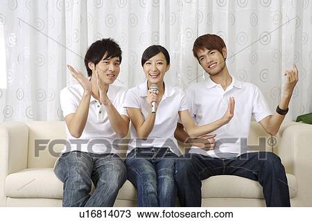 Stock Image - Three people sitting on sofa and singing together. Fotosearch