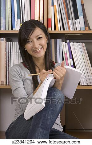 Picture - Young girl writing and sitting near bookshelf. Fotosearch