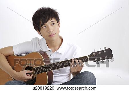 Stock Photograph - "Young man playing guitar and looking away, portrait". Fotosearch