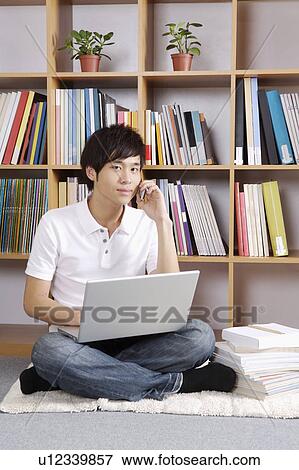 Stock Photo - Young man using laptop and on the phone. Fotosearch
