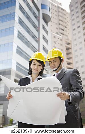 Stock Image - Businessman and businesswoman holding blueprint together. Fotosearch