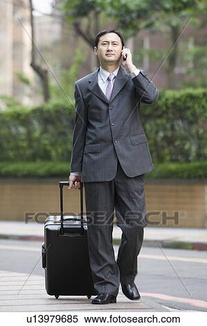 Businessman holding a suitcase and on the phone View Large Photo Image Stock Photography - Businessman holding a suitcase and on the phone. Fotosearch