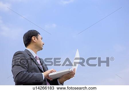 "Businessman holding laptop and looking away, portrait" View Large Photo Image Stock Image - "Businessman holding laptop and looking away, portrait". Fotosearch