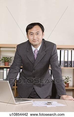 Stock Image - Businessman looking at the camera with hands on desk. Fotosearch