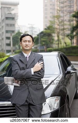 Stock Photo - Businessman standing with vehicle and holding newspaper. Fotosearch