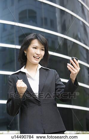 Businesswoman looking at mobile phone and smiling happily View Large Photo Image Picture - Businesswoman looking at mobile phone and smiling happily. Fotosearch