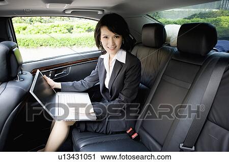 Stock Image - Businesswoman sitting in the car and using laptop. Fotosearch