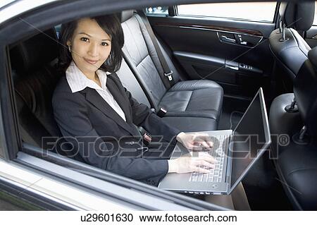 Stock Image - Businesswoman sitting in the car and using laptop. Fotosearch