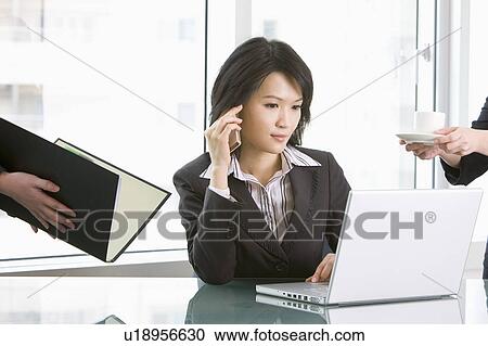 Stock Image - Businesswoman using laptop and on the phone. Fotosearch