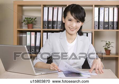 Stock Image - Businesswoman working in the office and smiling at the camera. Fotosearch